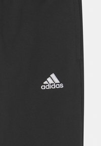 Svart tyg med vit broderad Adidas-logotyp som har tre snedställda ränder och ordet "adidas" nedanför.