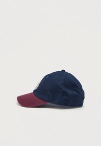 Gorra de béisbol azul marino con visera en color burdeos, que presenta un bordado en la parte frontal y ojales de ventilación en los lados.
