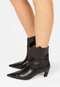 Black leather ankle boots with pointed toes, featuring western-style stitching and a short heel, showcasing a smooth texture and tailored fit.
