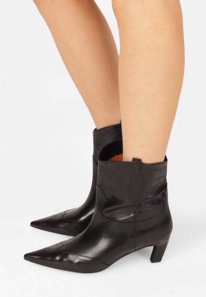 Black leather ankle boots with pointed toes, featuring western-style stitching and a short heel, showcasing a smooth texture and tailored fit.