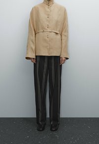 Beige ykk oversized jakke med en båndet liv, som har en høy krage og metallknapper. Kombinert med svart og gråstripete vide bukser.