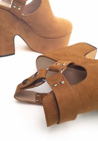 Scarpe con tacco alto in suede marrone, con piattaforma, punta aperta e cinturino alla caviglia con dettagli in argento e un tacco spesso a blocco.