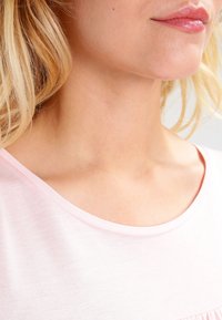 Jasnoróżowa koszulka z dekoltem w serek, miękka tekstura, krótkie rękawy i subtelne marszczenie na dole.