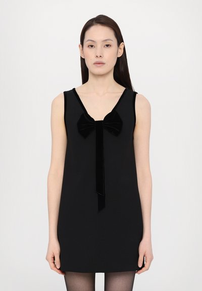 Robe noire sans manches avec un décolleté en V profond, ornée d'un grand nœud en velours et d'un accent en ruban au centre devant. Tissu lisse, silhouette en forme de A.