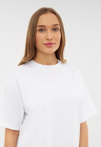 Camiseta de algodón blanca con mangas cortas y escote redondo, que presenta una textura suave y un diseño minimalista sin patrones.