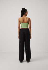 Zelený rebrovaný crop top s tenkými ramienkami, skombinovaný s čiernymi širokými nohavicami s elastickým pásom a mäkkou textúrou.