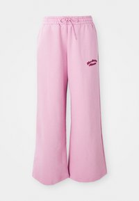 Pantalons de survêtement roses clair en tissu doux, présentant une coupe large, une taille élastique avec cordon de serrage et un détail de logo brodé.