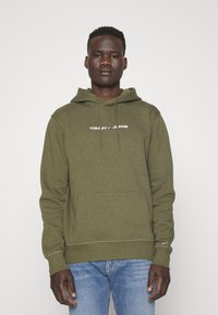 Sudadera de color verde oliva con un bolsillo frontal, capucha ajustable con cordón y el logo en blanco "TOMMY JEANS". Puños y dobladillo acanalados.