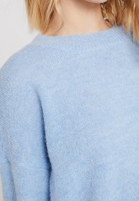 Pull bleu clair en maille, texture douce, encolure ronde, coupe oversize, présentant un aspect lisse et uniforme sans motifs ni accents visibles.