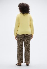 Rumeno pleten pulover z dolgimi rokavi, kombiniran z rjavimi in črnimi hlačami z izrazitimi črtami. Tekstura je gladka, hla�če pa imajo vzorec cik-cak.