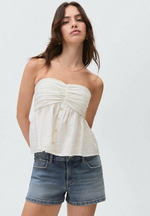 Weißes trägerloses Oberteil mit geraffter Textur und Knopfdetail vorne, kombiniert mit mittelblauen Denim-Shorts. Schlichtes Design, keine Muster oder Akzente.