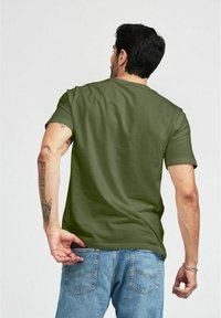 Olivgrön kortärmad t-shirt med rund halsringning, visad bakifrån, i kombination med ljusblå denimjeans.