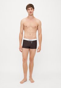Pantaloni de baie maro cu un cordon alb în talie, fabricați dintr-un material elastic, cu o croială strânsă și un design minimalist.