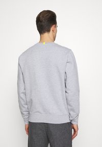 Felpa grigia con maniche lunghe, scollo rotondo, polsini e orlo a coste. Presenta un piccolo dettaglio giallo sul retro del collo.