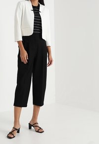 Vit kort blazer, svart och vit randig topp, svarta vida byxor och svarta sandaletter med remmar. Släta texturer, rena linjer och skräddarsydd passform.