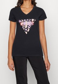 Camiseta negra de cuello en V con un gráfico en forma de triángulo que presenta letras multicolores en tonos de rosa, morado y rojo en el frente. Textura de tela suave.