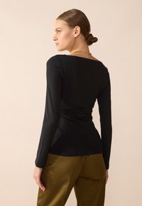 Svarte langermede topper med vid halslinje, tettsittende design og glatt tekstur, sammen med olivengrønne bukser. Minimalistisk stil.