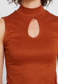 Top sin mangas de tejido acanalado en color óxido. Presenta un alto cuello y un corte en forma de lágrima en el cuello. Textura suave, diseño ajustado.