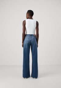 Jeans in denim a gamba larga di colore blu scuro con vita alta, dotati di tasche posteriori e un'etichetta in pelle beige. Abbinati a un top aderente bianco.