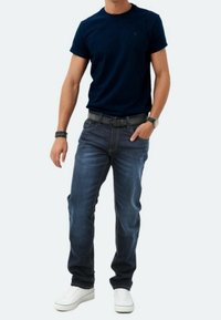 T-shirt navy a girocollo, abbinato a jeans blu scuro. Sneakers bianche e una cintura nera. La texture dei jeans è liscia con dettagli di cucitura sottili.
