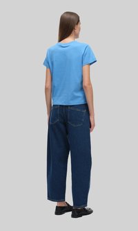 Niebieska bawełniana koszulka z krótkim rękawem zestawiona z wysokimi szerokimi dżinsami w ciemnoniebieskim kolorze. Czarne buty dopełniają całość.