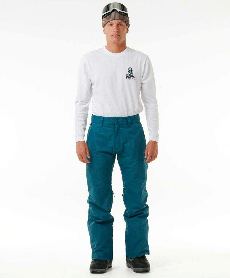 Teal sneeuwbroek met een losse pasvorm, ritsen aan de zijkanten, gecombineerd met een wit long sleeve shirt en een gebreide bruine beanie met een skibril.