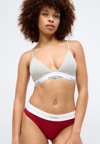 Hallutsinine puuvillane rinnahoidja õhukeste rihmadega ja valge ribaga, millel on "Calvin Klein"; punased soonikbikiinipüksid valge vöökohaga ja logoga.