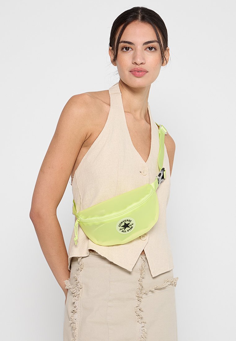 Riñonera de nailon verde lima con cierre de cremallera y logo de Converse, con una correa ajustable y una textura suave y brillante.