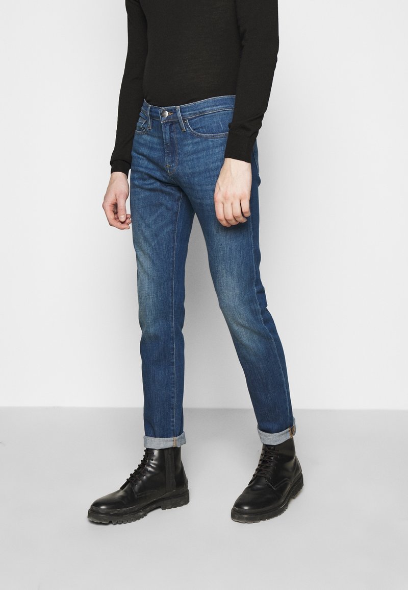 Smal passform i blå denimjeans med blekta områden, femficksdesign och uppvikta nederkanter, kombinerat med svarta snörstövlar och en svart åtsittande långärmad tröja.