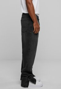 Dark grey jeans with a straight-leg design, featuring zipper accents at the cuffs and standard back pockets. Worn with white sneakers.