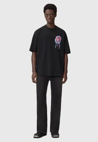 Mustvalge ülisuur t-särk, millel on värvikas tilkuv grafika rinnal, kombineeritud tumedate sirgete pükstega ja mustade jalatsitega.