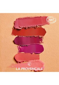 Quatre teintes de rouge à lèvres crémeux dans des nuances : rouge profond, rose rouge, fuchsia et corail, sur un fond texturé pêche. Logo de la marque en bas.