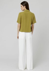 Chemise col montant à manches courtes de couleur vert olive associée à un pantalon blanc ample avec poches arrières et tissu texturé.