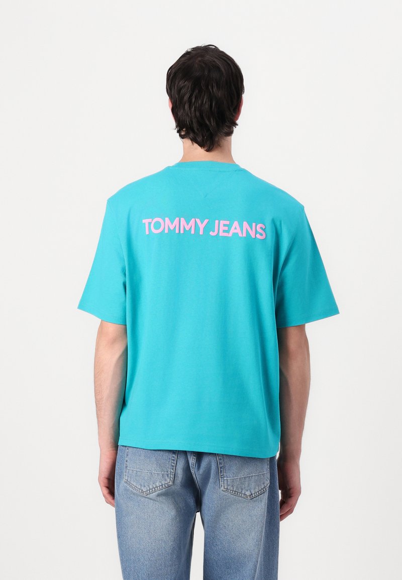 Turkio spalvos medvilninė marškinė su telefono „TOMMY JEANS“ uždaru rožinės spalvos ant nugaros. Trumpomis rankovėmis, laisvas kirpimas, minimalistinis dizainas.