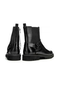 Botines negros de cuero con paneles laterales elásticos y detalle de correa ajustable. Presentan una suela gruesa y textura lisa.