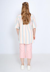 Chemise rayée aux couleurs pastel avec des manches courtes, associée à un pantalon court rose clair. Des chaussures décontractées complètent la tenue.