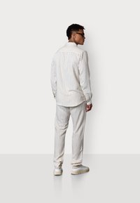 Weiß gestreiftes Hemd und passende Hose aus leichtem Material. Das Outfit hat einen lockeren Schnitt und wird mit hellen Sneakers kombiniert.