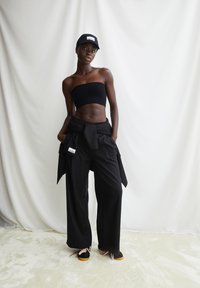 Zwarte cropped bandeau top gecombineerd met losse zwarte broek met een gestrikte taille en een capuchon. De schoenen zijn zwart met gekleurde veters en een bruine zool.