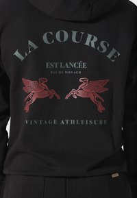 Sudadera negra con el texto "LA COURSE EST LANCÉE PAS DE MONACO VINTAGE ATHLEISURE" y gráficos de esqueletos de caballos alados rojos en la espalda.