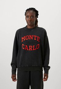 Zwarte oversized sweater met rode "MONTE CARLO" grafische tekst. Gemaakt van zacht materiaal met een ronde halslijn en geribbelde zoom en manchetten.