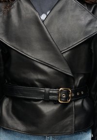 Μαύρο δερμάτινο μπουφάν με διπλό πέτο γιακά, διπλή σειρά κουμπιών και φαρδύ ζώνη με χρυσή αγκράφα και τρύπες. Λείο υφή.