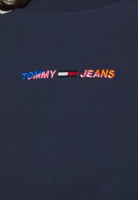 Camiseta de algodón azul marino con texto bordado multicolor "TOMMY" y "JEANS" con una línea horizontal separadora en el centro.