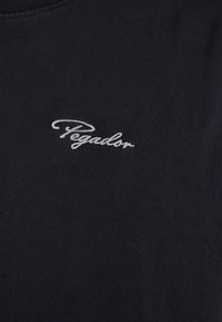 Camiseta negra de algodón suave con cuello redondo. Presenta un pequeño logo bordado en blanco que dice "Pegador" en el pecho.