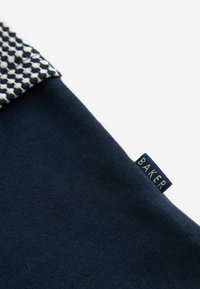 Navyfarbener Stofftop mit einem strukturierten Kragenmuster in Weiß und Marineblau. An der Seite ist ein blauer Anhänger mit dem Wort "BAKER" sichtbar.