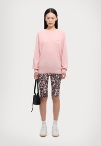 Maglione rosa chiaro con maniche lunghe e piccolo logo. Shorts da ciclismo leopardati neri e rosa. Sneakers bianche e piccola borsa nera.