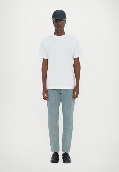 T-shirt en coton blanc, jeans bleus, casquette en cuir noire et mocassins noirs. Design simple avec des accents minimaux et une coupe décontractée.
