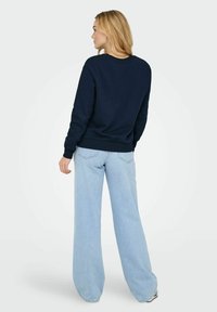 Sweatshirt bleu marine avec un col rond et des poignets côtelés, associé à un jean large bleu clair. Texture lisse et détails minimalistes.