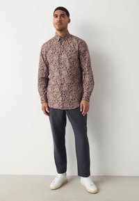 Camicia a maniche lunghe con motivo floreale in tonalità rosa sfumate, abbinata a pantaloni scuri e sneakers bianche; tessuto morbido con un taglio casual.