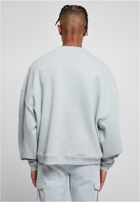 Felpa oversized azzurro chiaro con scollatura rotonda, spalle abbassate e polsini a costine. Texture morbida e vestibilità comoda.