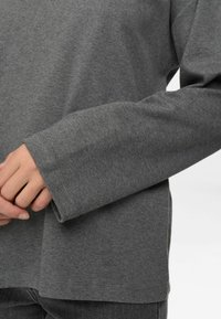 Hall kätkusega hall pikkade varrukatega särk, mis on valmistatud pehmest kangast, laia lõike ja laiade mansettidega. Särgil on sirge äärejoon ning nähtavaid mustreid või aktsente ei ole.